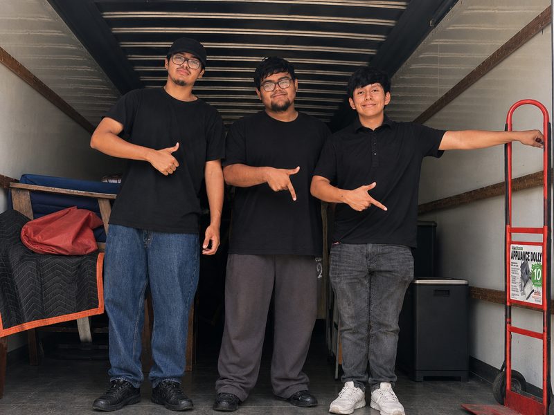 The Move It Clear It crew standing in the back of a moving truck with an appliance dolly and furniture pads