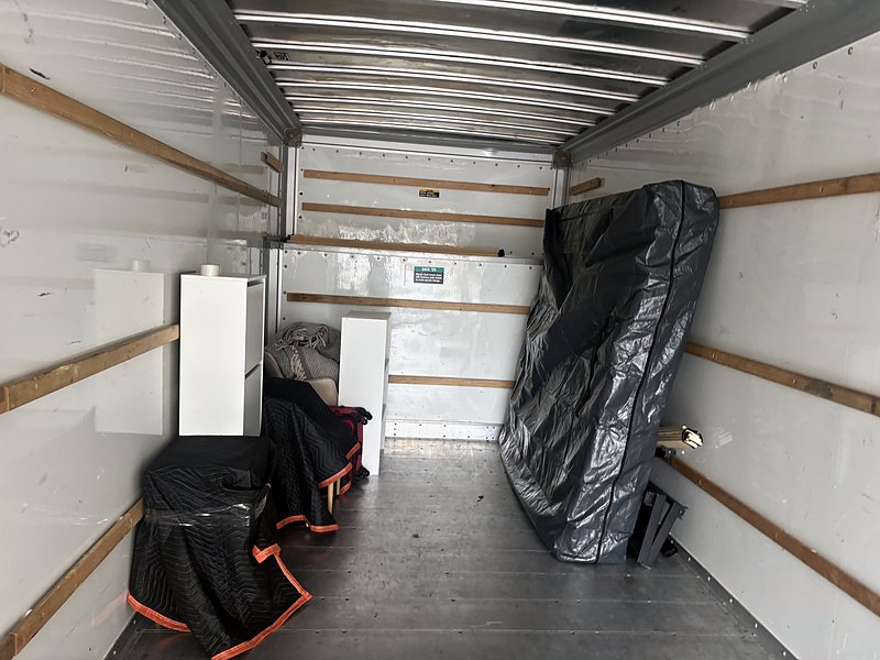 The inside of a customer's rental truck part-way through loading: a mattress in a protective bag stood against the wall, and furniture padded with moving blankets stacked along the side.
